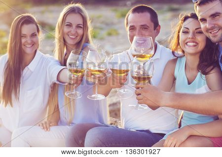 People holding glasses of white wine making a toast at the beach picnic