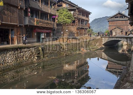 Zhaoxing Dong Village Guizhou Province China - April 8 2010: Rural River with cobblestone waterfront surrounded by wooden huts village minority.
