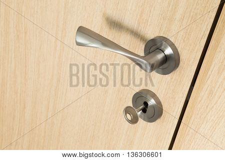 Metal door handle and key in a lock on a light wooden interior wooden door standing slightly ajar in a close up oblique angle view with copy space