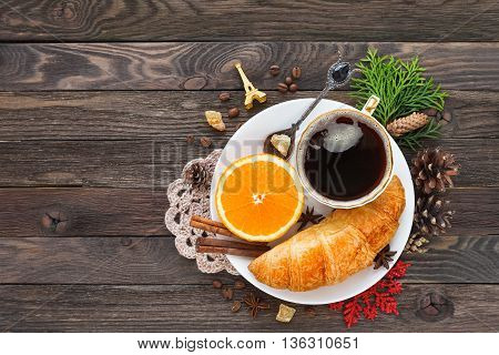 Continental breakfast - cup of hot coffee croissant and orange. Tasty food on rustic wooden background with Red snowflake and Eiffel tower. Cristmas and New Year food background. Top view place for text.