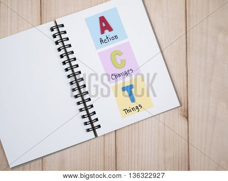Word spelling ACT and handwriting Action Changes Things" on white notebook with wood background (Business concept)