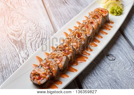 White plate with sushi rolls. Sauce of orange color. Meal served at sushi cafe. Recently cooked futomaki rolls.
