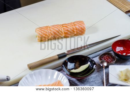 Sushi roll on cooking board. Knife lying beside sushi. Traditional uramaki rolls with salmon. Dish made of fresh ingredients.