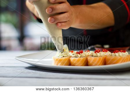 Sushi plate on wooden surface. Tool putting cream cheese. Chef makes uramaki rolls. Smoked salmon and red caviar.