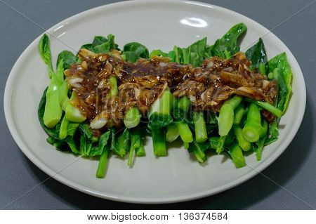 Kale fried in oyster sauce on white dish and background blue.