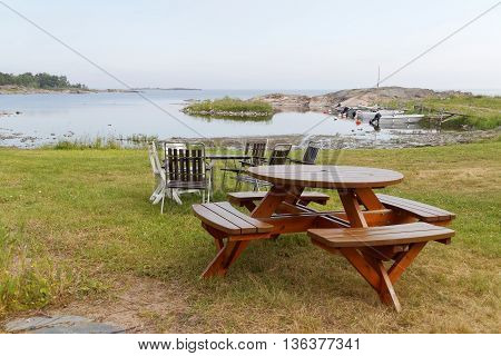 Group of tables and chairs small harbor boats and the sea in the background. No people