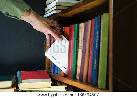 mans hand gets ebook among old paper books from the bookshelf. new technology concept