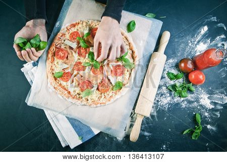 Hands of baker adding ingredients into pizza during pizza preparation at kitchen