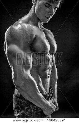 Muscular bodybuilder guy doing posing over black background. Naked torso in jeans. Close-up. Black and white, b w