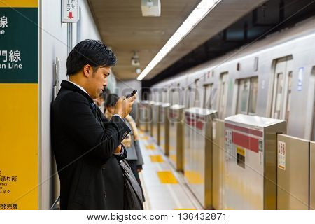 TOKYO JAPAN - NOVEMBER 28 2015: Unidentified Japanese subway commuter uses his device while waits for a train on a plateform