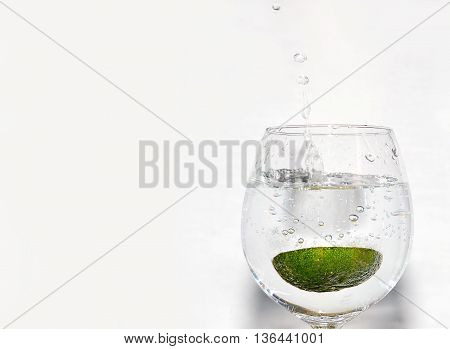 Slice of lime being dropped into a glass on white background on right hand side