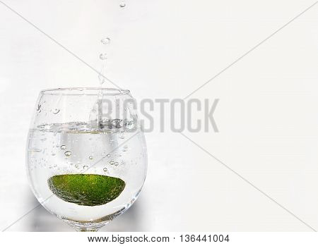 Slice of lime being dropped into a glass on white background on left hand side