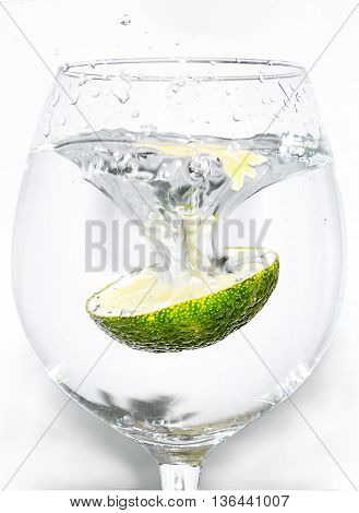 Slice of lime being dropped into a glass on white background