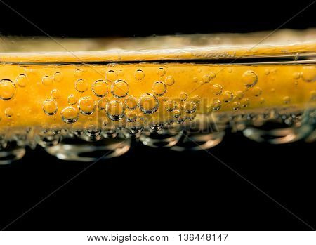 A slice of lemon in a glass of drink close up macro on black background