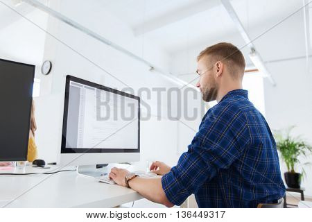 business, technology, education and people concept - young creative man or programmer with computer working at office