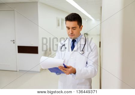 medicine, healthcare and people concept - doctor writing to clipboard at hospital