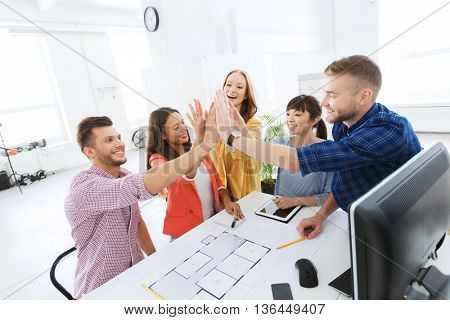 business, startup, architecture, gesture and people concept - happy international creative architect team or students with blueprint making high five at office