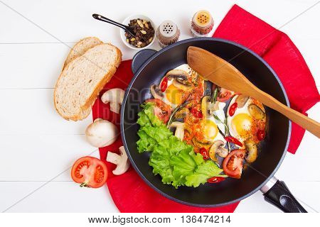 Fried eggs in pan with tomato bread pepper and mushrooms on wooden background