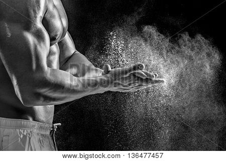 young muscular man preparing to hand lifting heavy weight. White talcum dynamically scatters in different directions. Black and white. stands sideways. Close-up