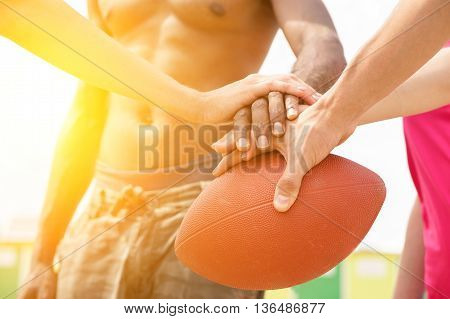 Multiracial friends playing rugby on the beach in sunny day - Multinational hands on top of oval ball - Summer sport against racism concept - Sunshine color tones with soft warm filte