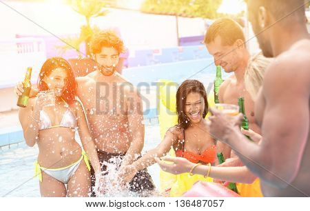 Group of multi ethnic friends having party in pool drinking cocktail and beer - Young people laughing and smiling outdoor in summer time - Vacation and friendship concept - Soft focus on left guy
