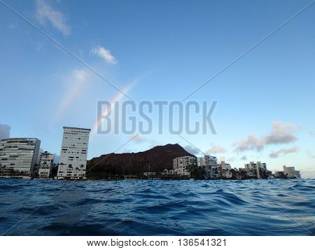 Double Rainbow over Hotel building Outrigger Canoe Club coconut trees Condo buildings clouds and Diamond Head Crater in the distance on Oahu Hawaii viewed from the water on a beautiful day.