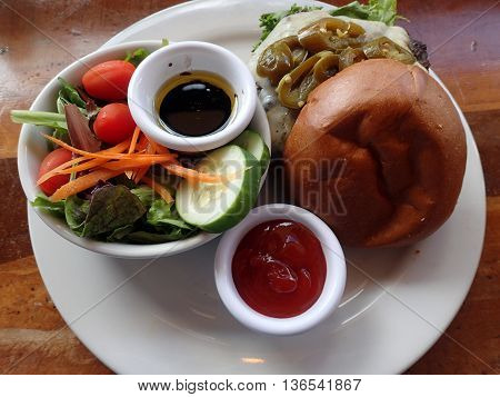Open jalapeno Pepperjack Cheeseburger with salad featuring lettuce tomatoes cucumbers Carrots with oil and vinegar and side of ketchup.