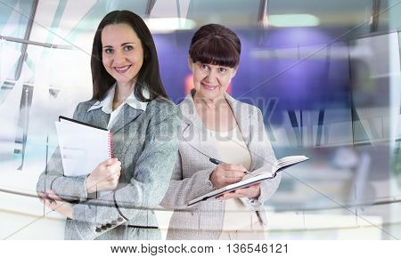 Attractive mature age woman and young businesswoman in office against of glass reflection