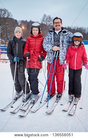 Family portrait of four skiers standing at ski resort in evening.