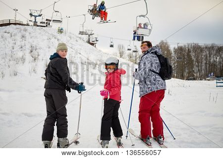 Man with two children look backwards while ski to cableway in winter day at ski resort.