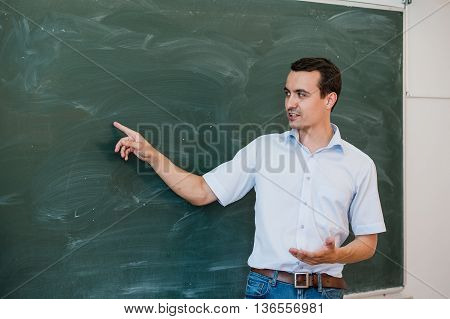 Young male teacher pointing at blackboard and talking.