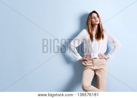 Beautiful young woman in a white shirt and beige pants on blue wall background