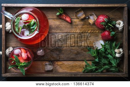 Homemade strawberry lemonade with mint and ice, served with fresh berries in woodentray, top view, copy space. Food frame