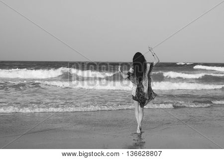Young beautiful woman brunette with long dark hair in red white tunic dress gold bracelets entering the Indian Ocean at sunset. Romantic style. Fashion model shot. Romance. Bohemian boho chic. Hippie style. Dreaming. Black and white image.
