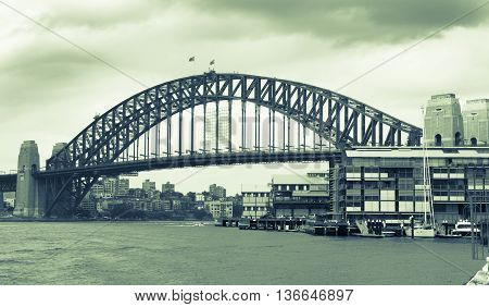 Old style image of Sydney Harbor Bridge Australia with darkening rain clouds gathering above split tone image green hue