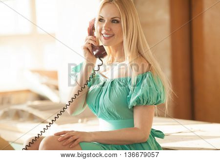 pretty blonde woman in green dress talking on old telephone. Fashion model. Sunny color.