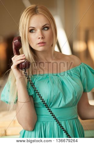 pretty blonde woman in green dress talking on old telephone. Fashion model. Sunny color.