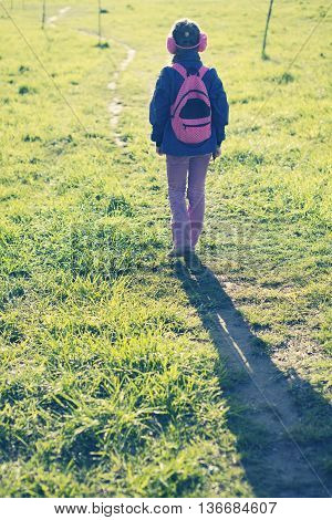 girl in ear muffs with backpack walking away by winding pathway
