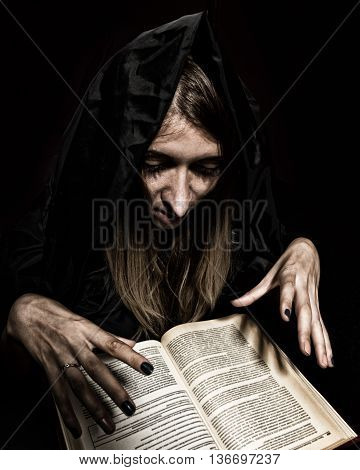 pretty witch casts spells from thick ancient book by candlelight on a dark background.