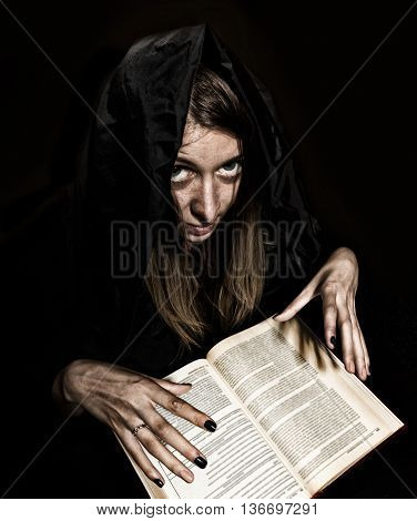 pretty witch casts spells from thick ancient book by candlelight on a dark background.
