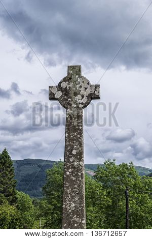 Ancient High Celtic Cross inscribed with biblical verse in Gaelic with backdrop of iconic Scottish scenery.