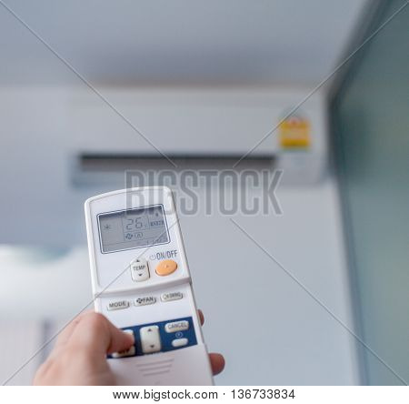 Left hand holding remote air conditioner turn up to 26 celcius with air conditioner blurred background