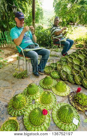 VALLE DE VINALES - CUBA JUNE 18, 2016: Cuban men weave palm leaves to make attractive baskets for sale to tourists visiting the famous caves at Cueva del Indio in the San Vicente Valley.