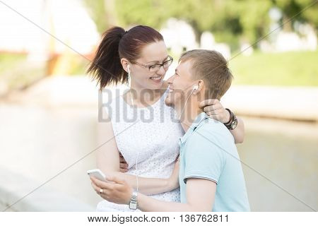 A Couple Sitting In The Park And Listening To Music On The Phone