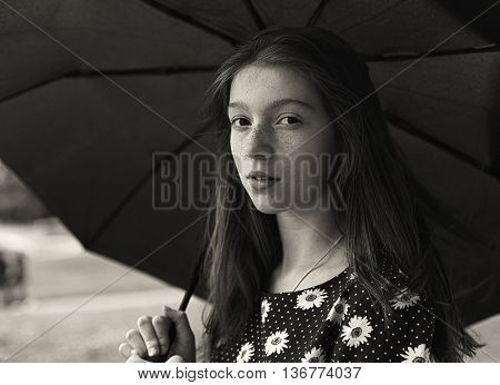 Black and white portrait of a pretty girl with freckled. Standing under umbrella.