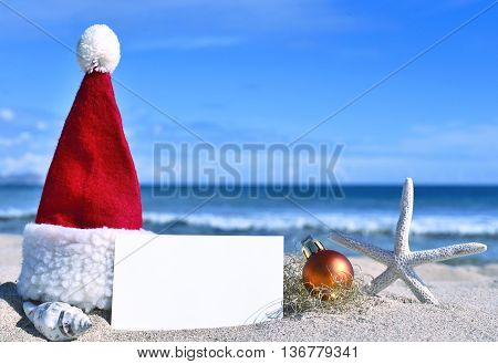 Blank white card with christmas decoration and sea shell on a tropical beach. Christmas holidays. Greeting card with copy space on the beach.
