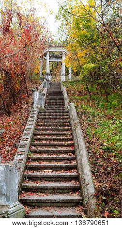 Old stairs to the gazebo in autumn park among yellow and red trees