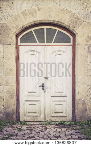 Old distressed white doors with coblestone path leading to it