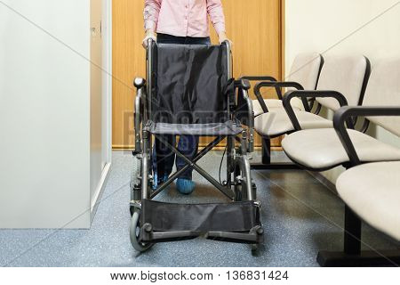 woman holding on to handle wheelchairs standing in lobby of hospital ready to transport patient