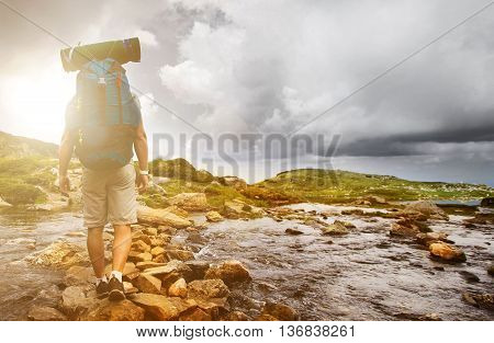 Hiker man with backpack crossing a river on stones in bulgarian mountains. Hiking and leisure theme. Image with sunlight effect